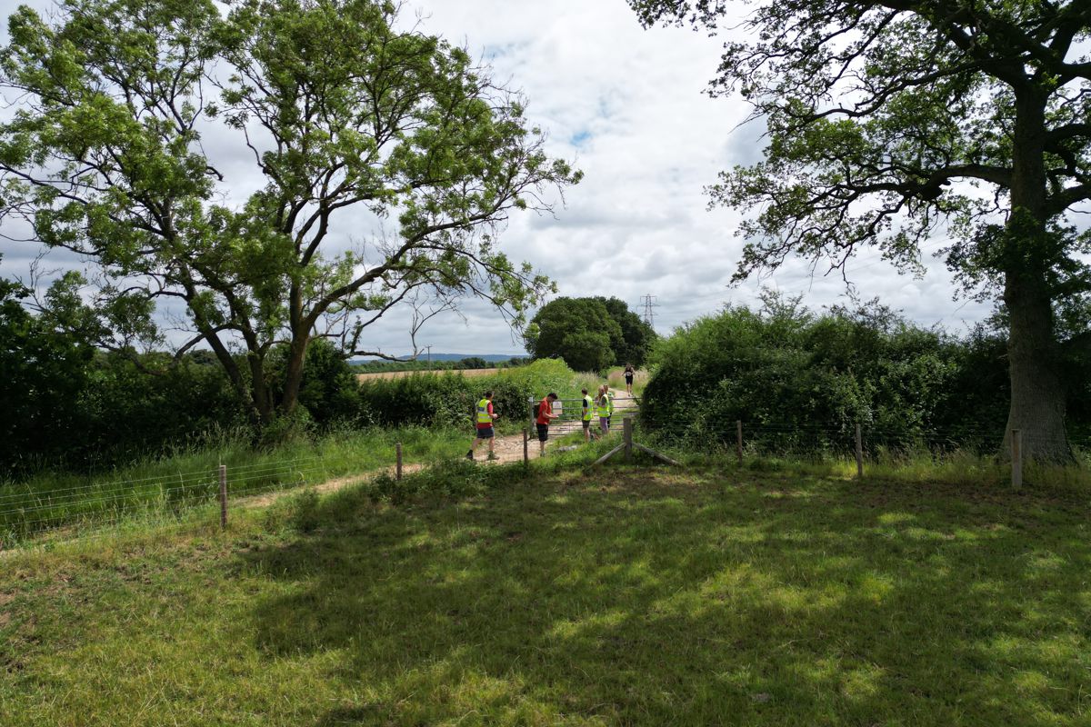 Marshals at a field gate on the course with farmland beyond
